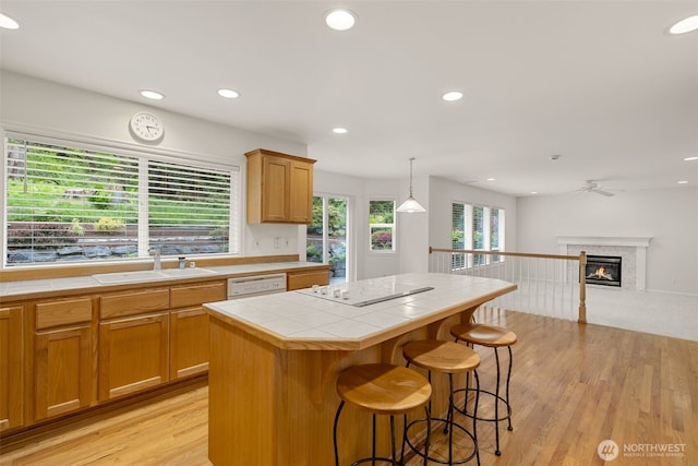 kitchen with tile countertops, a sink, white appliances, light wood finished floors, and a glass covered fireplace