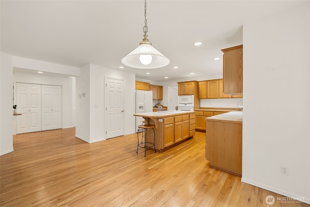 kitchen featuring white appliances, light countertops, a kitchen island, light wood finished floors, and recessed lighting