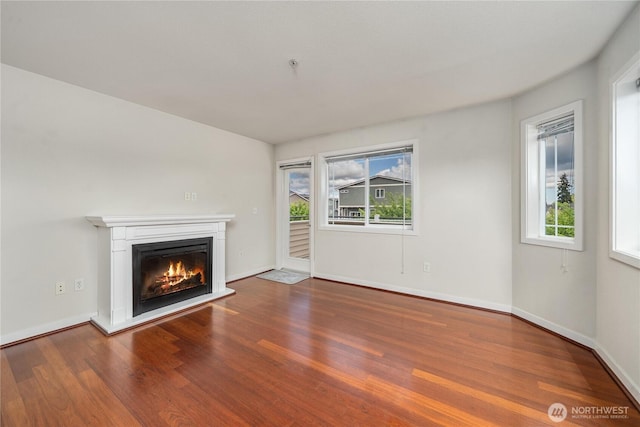 13426 97th Ave E Unit 303, Puyallup, WA 98373 - unfurnished living room featuring plenty of natural light, wood finished floors, a glass covered fireplace, and baseboards