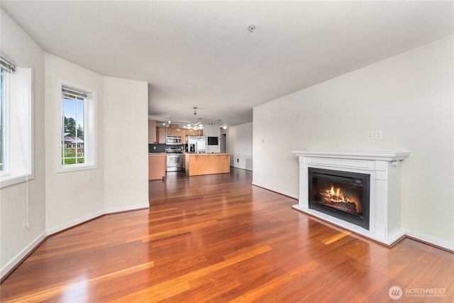 13426 97th Ave E Unit 303, Puyallup, WA 98373 - unfurnished living room with a glass covered fireplace, dark wood-type flooring, a chandelier, and baseboards