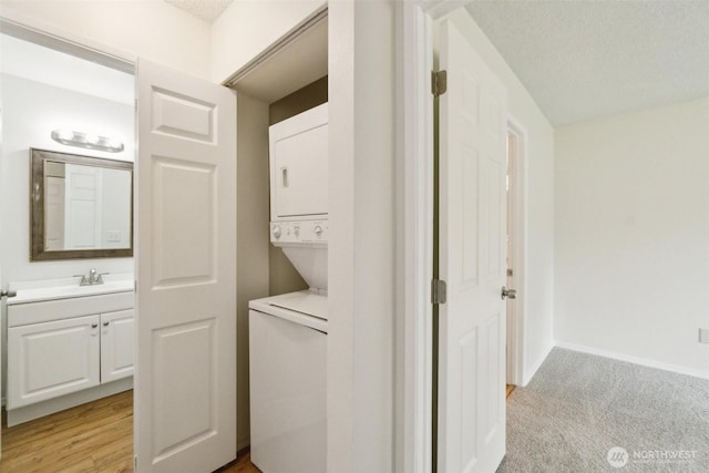 washroom featuring stacked washer / dryer, baseboards, a textured ceiling, and light colored carpet