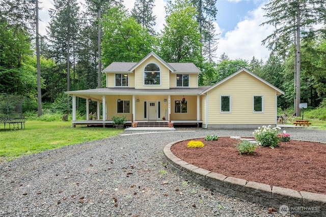 view of front of home featuring driveway, covered porch, a trampoline, a front yard, and view of wooded area