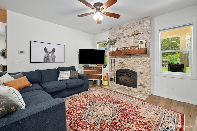 living room featuring wood finished floors, a ceiling fan, a stone fireplace, and baseboards