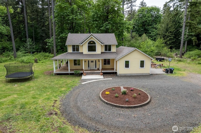farmhouse with a trampoline, curved driveway, a front lawn, a porch, and a wooded view