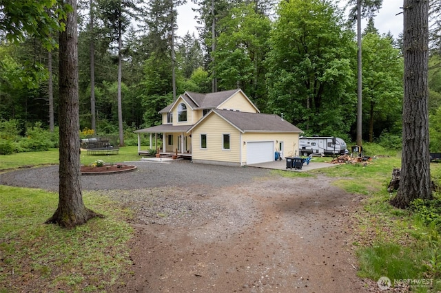 view of front of house with driveway, covered porch, a front yard, an attached garage, and a wooded view