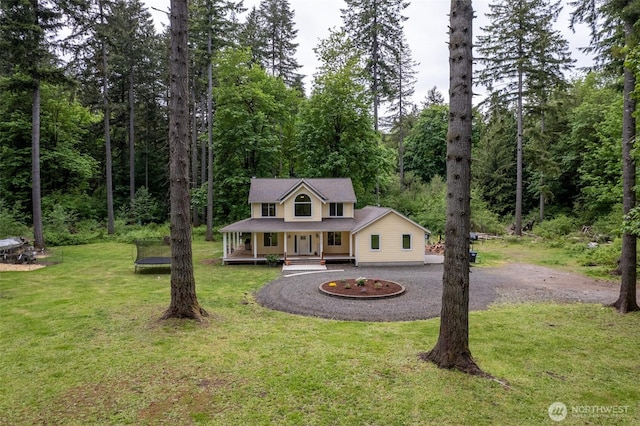 farmhouse inspired home featuring covered porch, a front lawn, a view of trees, and curved driveway