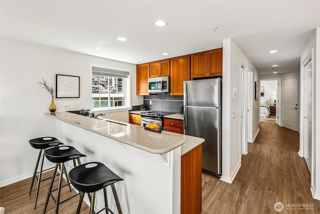 2432 Dexter Ave N Unit 201, Seattle, WA 98109 - kitchen featuring stainless steel appliances, a kitchen breakfast bar, brown cabinets, recessed lighting, and baseboards