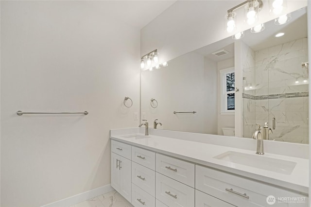 bathroom featuring toilet, marble look tile flooring, baseboards, a marble finish shower, and double vanity