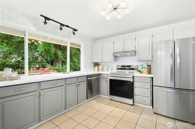 kitchen with stainless steel appliances, gray cabinetry, under cabinet range hood, light tile patterned flooring, and light countertops