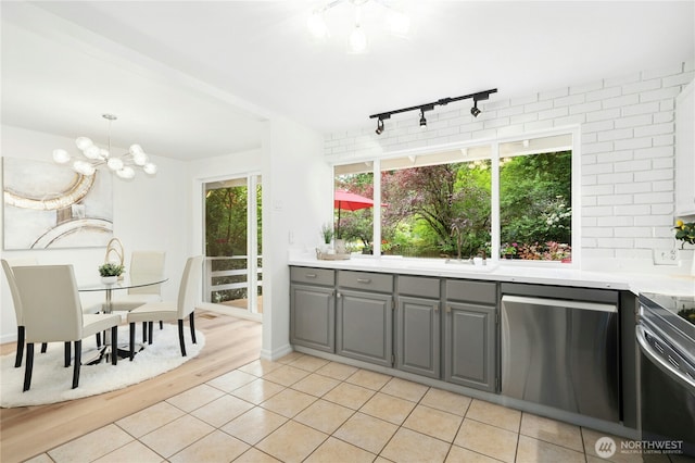kitchen with gray cabinetry, stainless steel dishwasher, a sink, track lighting, and a chandelier