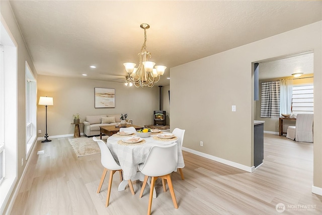 dining area with a wood stove, light wood-style flooring, a chandelier, baseboards, and recessed lighting