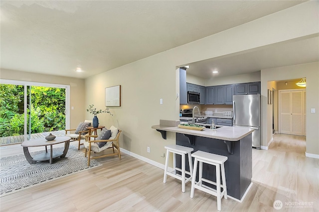kitchen featuring appliances with stainless steel finishes, light wood finished floors, light countertops, a breakfast bar area, and a peninsula