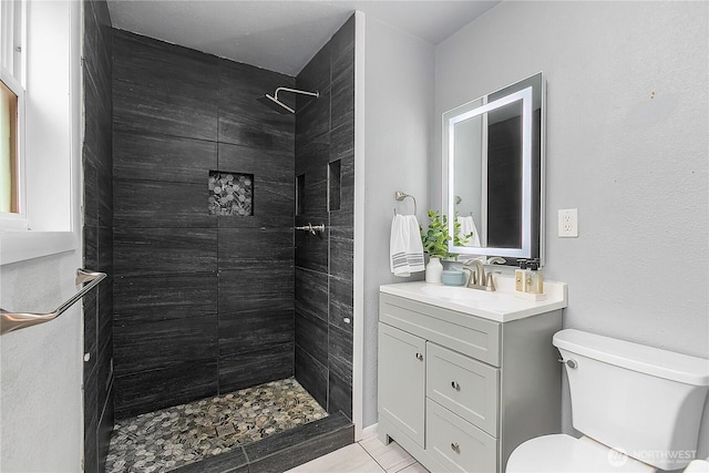 full bathroom featuring a tile shower, toilet, vanity, and tile patterned floors