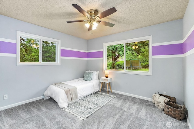 carpeted bedroom with multiple windows, baseboards, a textured ceiling, and a ceiling fan