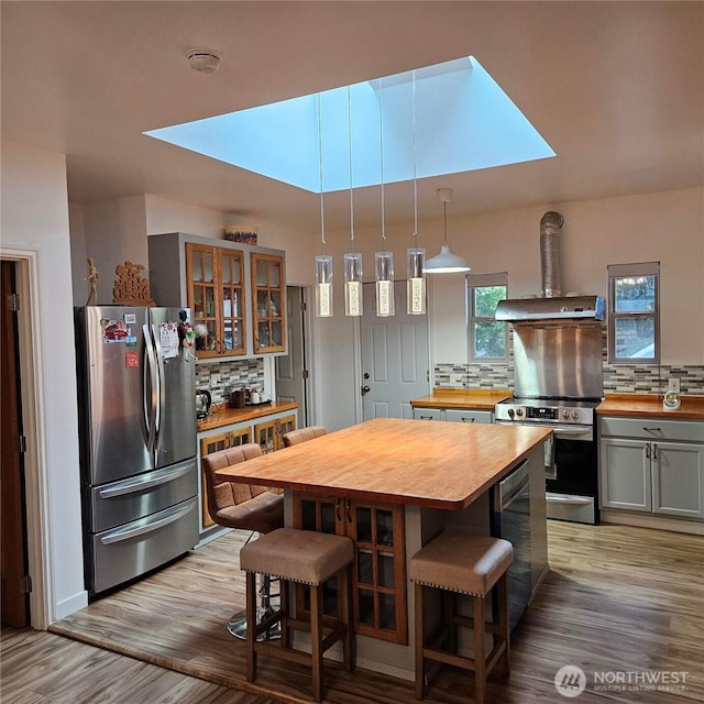 5830 115th Pl NE, Kirkland, WA 98033 - kitchen with butcher block countertops, stainless steel appliances, tasteful backsplash, light wood-style flooring, and glass insert cabinets