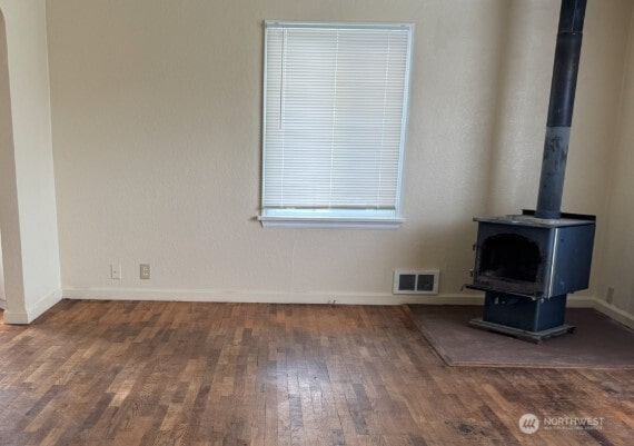 unfurnished living room featuring a wood stove, wood finished floors, and baseboards