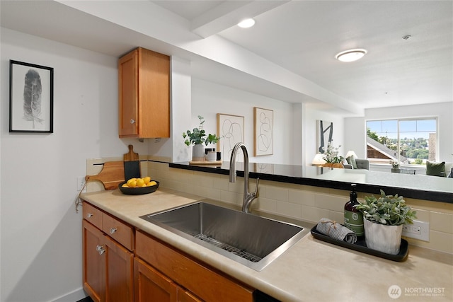 kitchen featuring a sink, brown cabinetry, light countertops, and backsplash