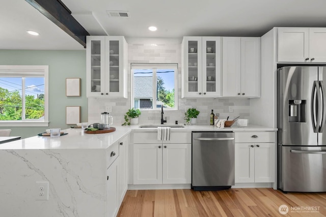 kitchen featuring appliances with stainless steel finishes, a sink, a peninsula, white cabinets, and recessed lighting