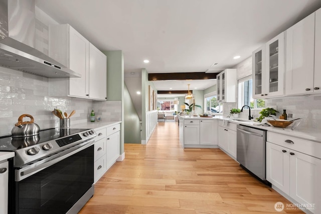 kitchen with appliances with stainless steel finishes, wall chimney exhaust hood, tasteful backsplash, light countertops, and light wood finished floors