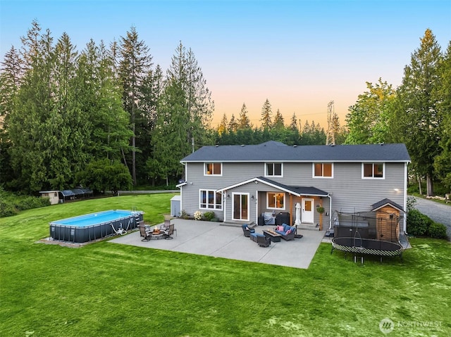 12915 212th St SE, Snohomish, WA 98296 - back of property at dusk with a trampoline, an outdoor pool, a patio area, a lawn, and an outdoor living space with a fire pit