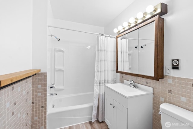 full bathroom with tile walls, shower / tub combo with curtain, toilet, vanity, and a wainscoted wall