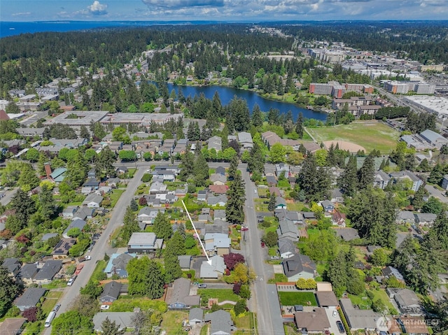 view of property location with a forest, a nearby body of water, and nearby suburban area