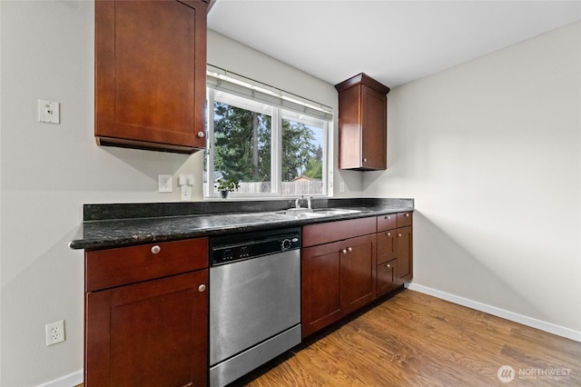 kitchen with stainless steel dishwasher, dark countertops, light wood finished floors, baseboards, and a sink