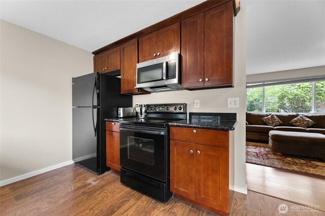 kitchen with black appliances, wood finished floors, dark stone counters, baseboards, and open floor plan