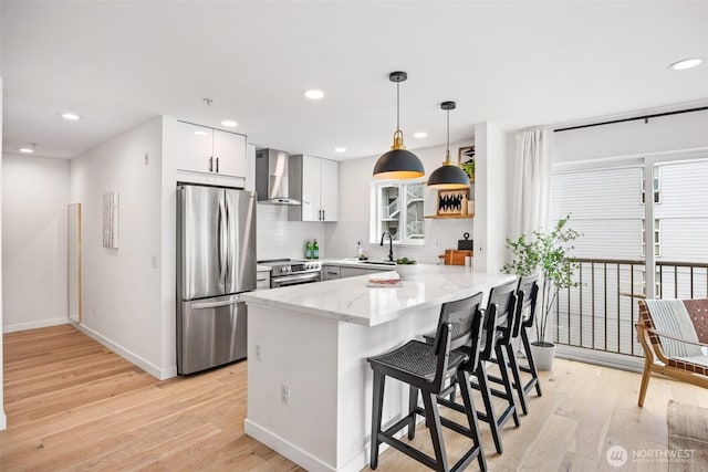 323 Queen Anne Ave N Unit 502, Seattle, WA 98109 - kitchen featuring stainless steel appliances, wall chimney exhaust hood, a peninsula, light wood-style floors, and light stone counters