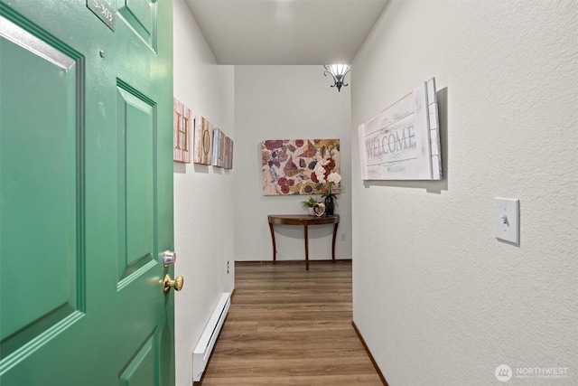 corridor with baseboard heating, wood finished floors, and a textured wall