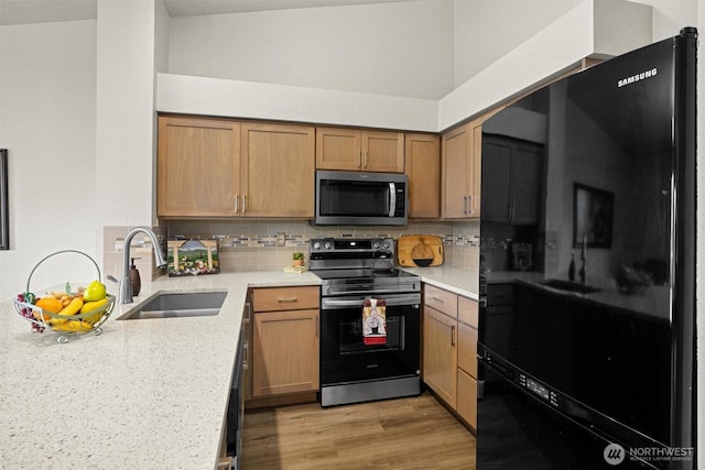 kitchen featuring stainless steel appliances, a sink, decorative backsplash, light wood-style floors, and brown cabinets