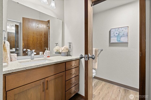 bathroom with wood finished floors, toilet, vanity, and baseboards