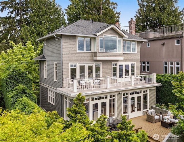 back of property featuring french doors, a chimney, roof with shingles, a wooden deck, and an outdoor hangout area