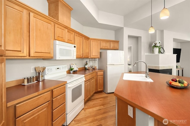 kitchen featuring white appliances, a sink, light wood-style flooring, and hanging light fixtures