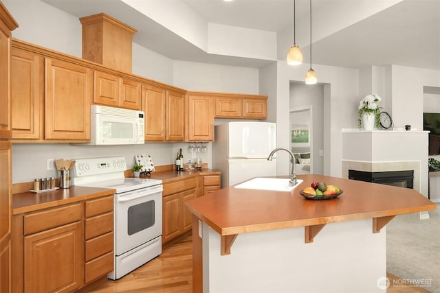 kitchen with white appliances, a sink, a kitchen bar, a center island with sink, and pendant lighting