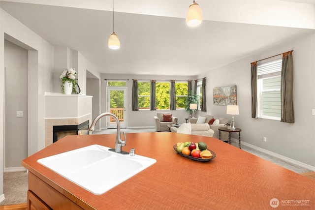 kitchen featuring a sink, baseboards, open floor plan, a tiled fireplace, and decorative light fixtures