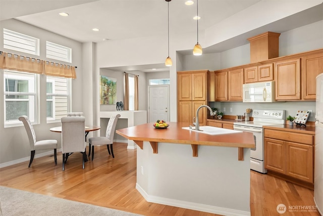 kitchen with white appliances, a sink, a center island with sink, a kitchen bar, and recessed lighting