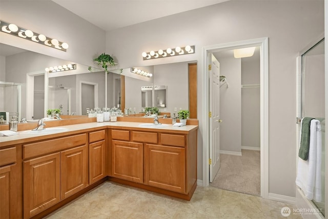full bathroom featuring a shower with door, double vanity, a walk in closet, and baseboards