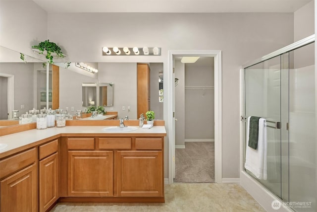full bath with a stall shower, double vanity, a spacious closet, and baseboards