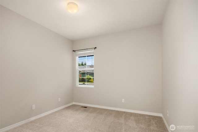 spare room featuring light colored carpet and baseboards