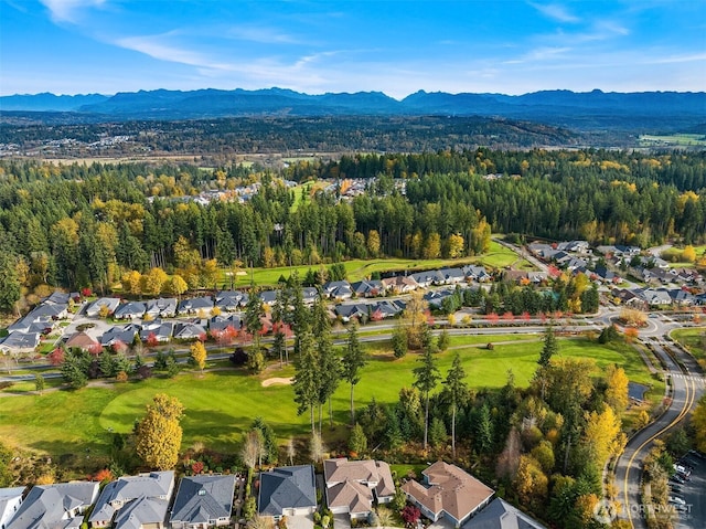 aerial view of property and surrounding area featuring nearby suburban area, a mountain backdrop, and a heavily wooded area