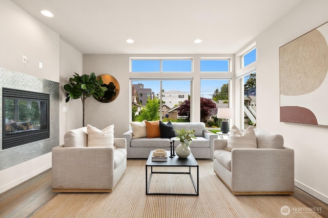 living area featuring wood finished floors, baseboards, recessed lighting, and a glass covered fireplace