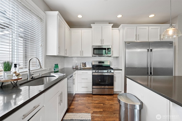 kitchen with appliances with stainless steel finishes, a sink, dark wood-type flooring, white cabinets, and dark countertops