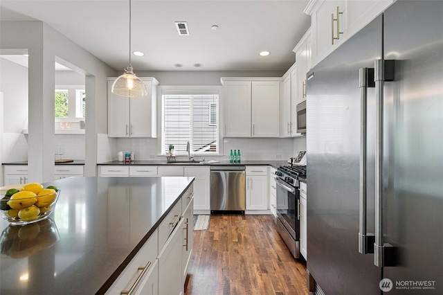 kitchen with stainless steel appliances, dark countertops, a sink, dark wood-style floors, and tasteful backsplash