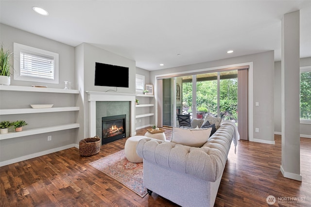 living area with a tiled fireplace, dark wood-style floors, baseboards, recessed lighting, and built in shelves