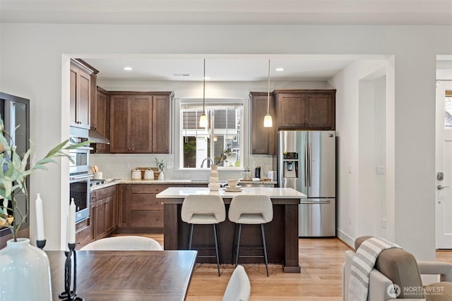 kitchen featuring stainless steel appliances, a center island, decorative backsplash, light countertops, and a breakfast bar area