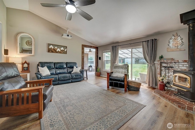 living room with a wood stove, a ceiling fan, vaulted ceiling, and wood finished floors