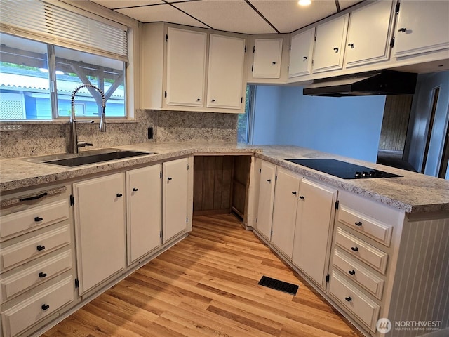 kitchen featuring black electric cooktop, a sink, light wood finished floors, light countertops, and decorative backsplash