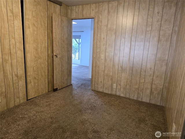 unfurnished room featuring carpet and wood walls