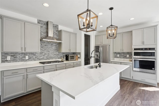 kitchen featuring wall chimney range hood, gray cabinetry, appliances with stainless steel finishes, tasteful backsplash, and a chandelier